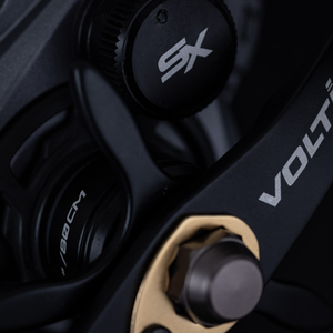 Close-up of the side of the VoltiQ SX reel in black and dark grey with gold accents, featuring the VOLTIQ brand name and an SX model marking.