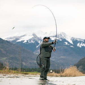 Man fishing at the side of a river, using an Abu Garcia Fishing Rod, with mountains in the background