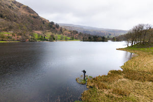 Person fishing from the side of the lake surrounded by hills and trees on a cloudy day