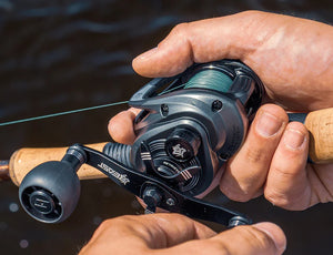 Close-up of a hand holding an Abu Garcia Beast Baitcasting fishing reel with water in the background